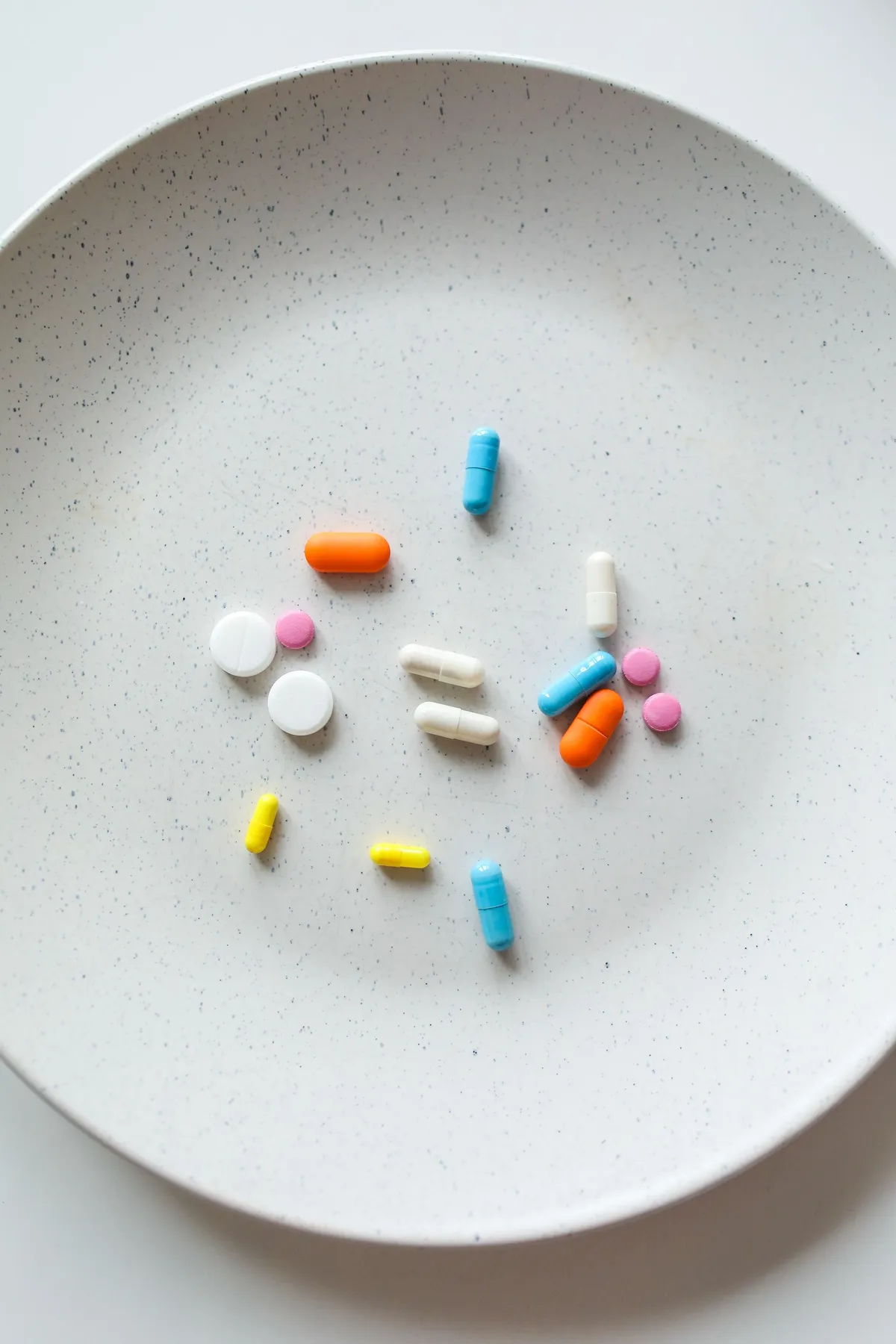Assorted medications on a white plate representing symptom-focused treatment compared with understanding metabolic health and underlying physiology.